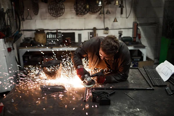 年轻的铁匠站在铁锤旁 用电动工具焊接或加工铁制工件 — 图库照片