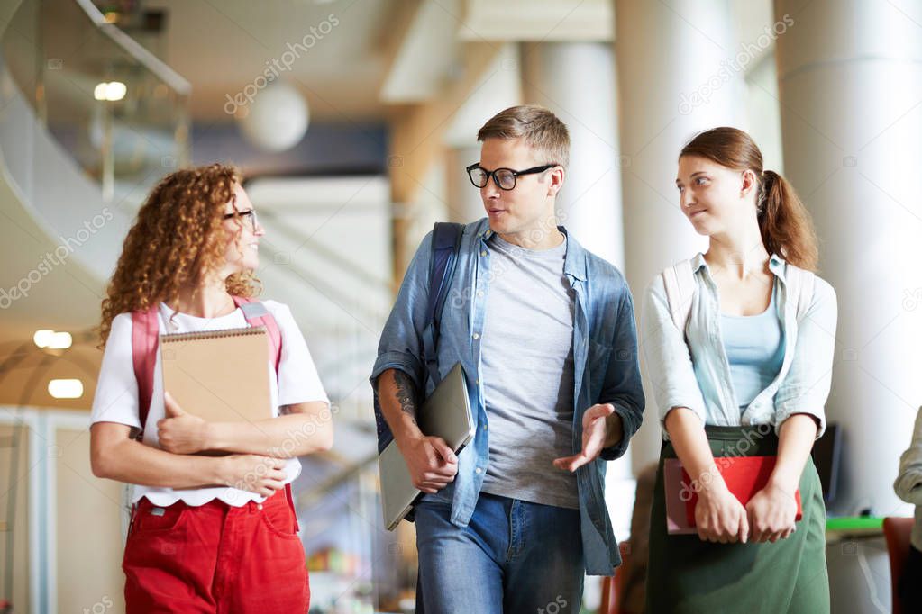 Guy and two girls in casualwear walking for the first lesson and discussing college news in the morning