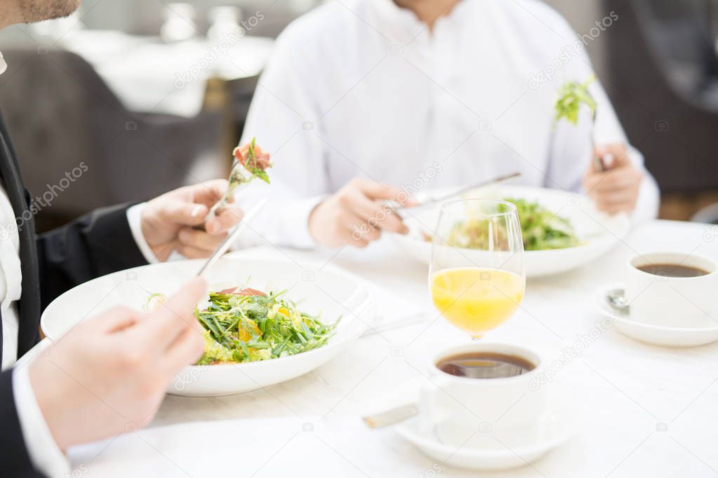 Businessman eating salad and having orange juice by lunch with colleague in restaurant