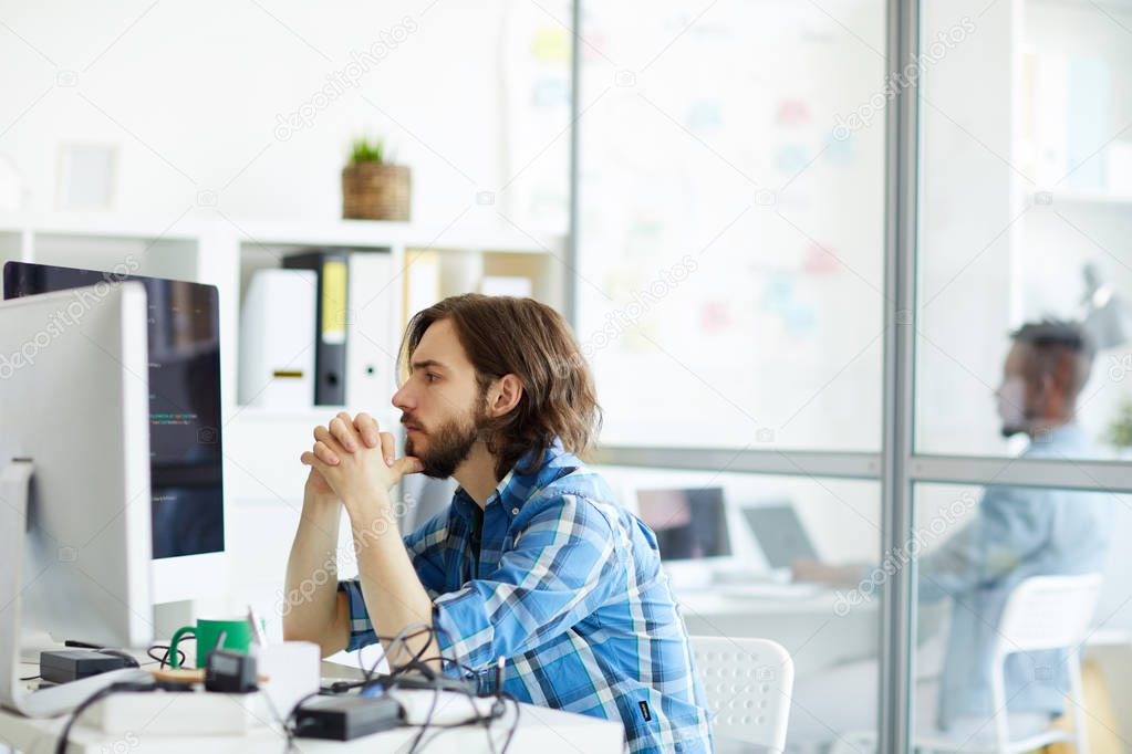 Serious it-manager concentrating on reading data on computer screen while sitting in office