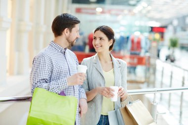 Genç alışveriş torbaları ve büyük çağdaş alışveriş merkezinde konuşmayı içecekler ile