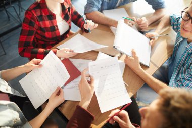 Modern ofiste ki toplantıda başlangıç projesi üzerinde işbirliği yaparken fikirleri tartışan yaratıcı iş ekibinin yüksek açılı kırpma çekimi, belgeleri masaüzerinde tutan ellere odaklanın