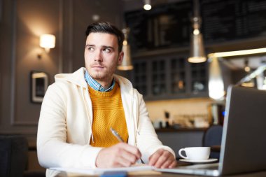 Kafede oturan, not lar alan ve dizüstü bilgisayarın önünde içki içen ciddi ve dalgın öğrenci