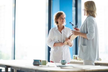 Not defteri olan genç yaratıcı kadın ve orta yaşlı meslektaşı organizasyon anlarıyla ilgili danışmanlık yapıyorlar.