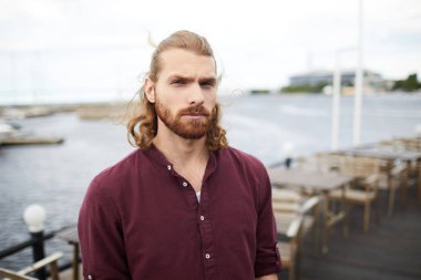 Çağdaş açık kafede, su kenarında duran tişörtlü genç adam.