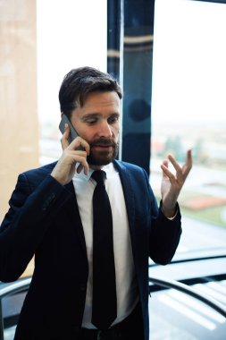 Ofiste çalışırken akıllı telefonla bir şeyler açıklayan formalgiyimli zarif işadamı