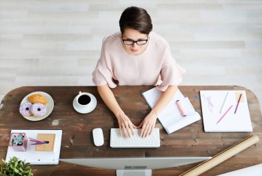 Young elegant businesswoman sitting in front of computer monitor, typing and searching for new creative ideas