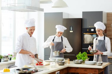 Meşgul şef ve aşçılar mutfakta çalışan ve tezgahta makarna pişirme: şef domates kesme, apron kontrol spagetti genç adam, ciddi bayan kırbaçmalzemeleri