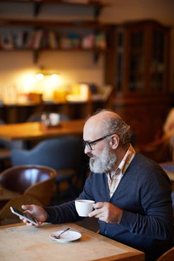 Gadget ve fincan çay ya da kahve tablo ve manifatura rahat kafede oturan ile üst düzey sakallı adam