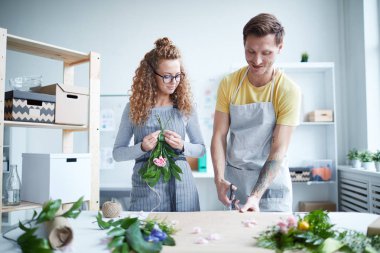 Çiçekçilerden biri ambalaj kağıdı keserken, yanında çiçek demeti olan meslektaşı