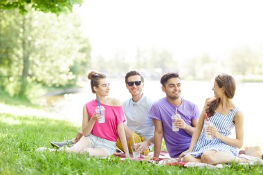 Yaz günü parkta yeşil çimenler üzerinde otururken sohbet içecekler ile dört gençler