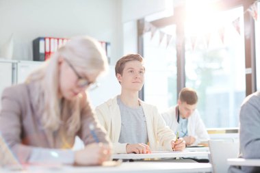 Akıllı adam masa başında otururken ve notlar yaparken tahtaya bakıyor ya da öğretmeni dinliyor.