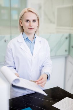 Üniformalı genç, kendinden emin klinisyen tıbbi belgeleri gösterirken sana bakıyor.