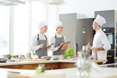Restoran mutfağında şefle birlikte yeni menü oluştururken üniformalı yemek pişirme arkadaşları