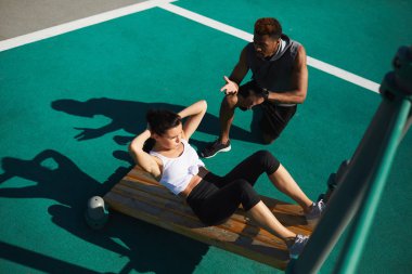 Diz üstü duran ve egzersizi yapan kadın tavsiye verirken el eller ciddi emin yakışıklı genç Afro-Amerikan fitness eğitmeni