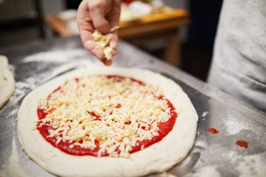Çiğ haddelenmiş pizza hamuru domates ketçap ve rendelenmiş peynir üzerinde insan eli ile üstüne