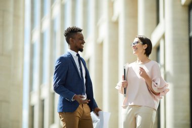 Neşeli heyecanlı genç çok ırklı meslektaşları konuşurken gülüyor ve yaz gezintisi sırasında modern binanın yakınında konuşurken