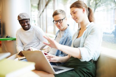 Genç bir kadın dizüstü bilgisayarında fikirlerini sunuyor ve erkeklere bazı verileri açıklıyor.