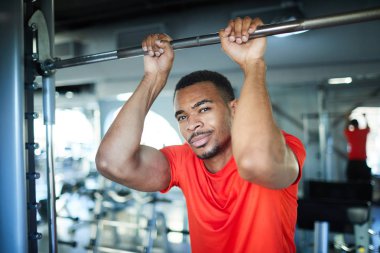 Kırmızı t-shirt üzerinde çelik spor bar modern fitness merkezinde egzersiz sırasında asılı etkin Afrikalı-Amerikalı atlet