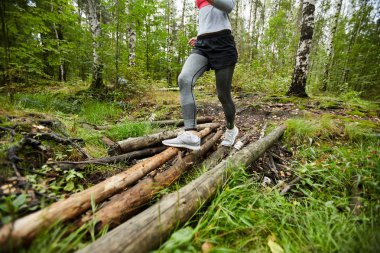 Aktif giyimli genç bir bayan sabah antrenman yaparken orman yolunda bir sürü kütük taşıyor.