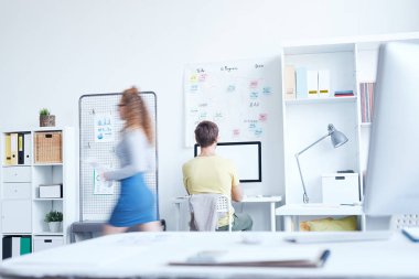 Genç ofis müdürü bilgisayarın başında oturuyor. Bulanık meslektaşı da yanından geçiyor.