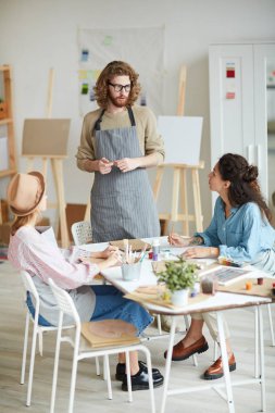 Genç kendine güvenen koç masa başında duruyor ve öğrencilere modern sanat ve resim öğretiyor.