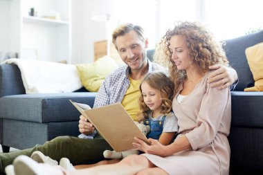 Üç kişilik genç bir aile boş vakitlerinde kanepede otururken masal okuyorlar.