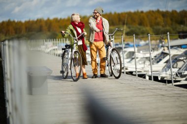 Güneşli sonbahar gününde bisikletlerle köprüden yürürken genç aşk Kafkas çift konuşan ve neşeli gülümseyen