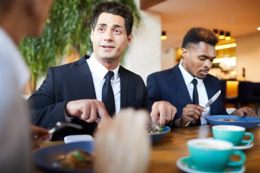 Restoranda akşam yemeğinde meslektaşları ile sohbet ederken resmi takım elbiseli pozitif yakışıklı genç işadamı masada oturan ve salata yerken