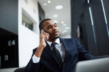 Afro-Amerikan etnik kökenden emin genç işadamı iş yerinde akıllı telefon ile konuşan