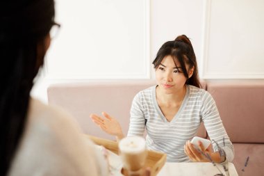 Kafeteryada siparişini beklerken rahatsız bir şekilde garsona bakan akıllı telefonlu memnun olmayan müşteri