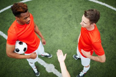 İki genç futbolcular avuç holding bozuk para veya aralarındaki çip ile bir başka karşısında yeşil sahada ayakta