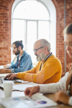 Gri sakallı kıdemli adam onun iş arkadaşları arasında b ydesk oturan ve net tarama