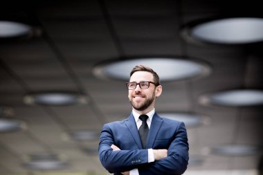 Genç, başarılı, iş elbiseli, gözlüklü, el ele tutuşan, bulanık arka plana bakan, gülen erkek.