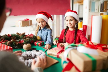 Noel Baba şapkalı iki küçük kız anneleri ile Noel için hediyeler hazırlanıyor