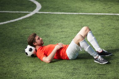 Yeşil sahada futbol topu onun boyun arkasında yatan genç dinlendirici futbolcu