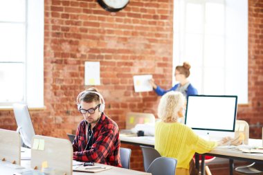 Bilgisayara veri girerken notlarına bakan kulaklıklı ciddi genç ofis çalışanı