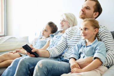Genç bir aile ve iki küçük kız kanepede oturup televizyon izliyorlar.