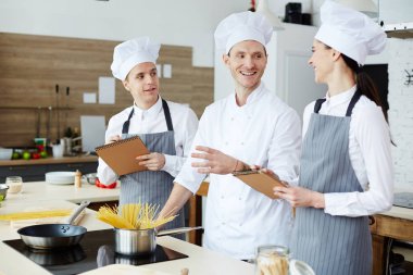 Makarna tarifi tartışırken üniformaneşeli kendinden emin pişirme uzmanları: öğrencilere spagetti kaynatın nasıl açıklarken yetenekli yakışıklı şef gesturing