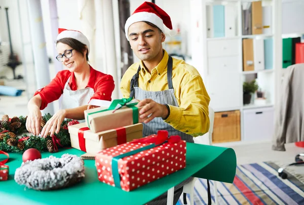 Jonge Kerstman Werkkleding Maken Stack Van Giftboxen Terwijl Zijn Collega — Stockfoto