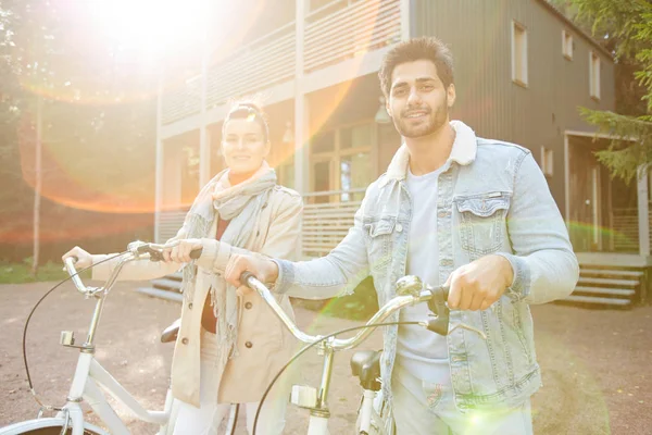 カジュアルな服を着た陽気な美しい若いサイクリストのカップルが一緒に自転車で歩き 屋外で日光の下でカメラを見て — ストック写真