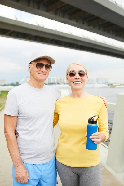 Senior Para Activewear Okulary Przeciwsłoneczne Obejmując Patrząc Kamery Treningu Zewnątrz — Zdjęcie stockowe