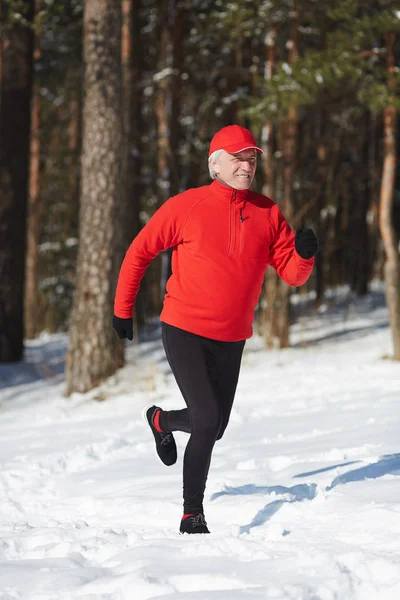 フォレスト をトレーニングしながら冬の日に雪の吹きだまりを実行しているアクティブな年配の男性 — ストック写真
