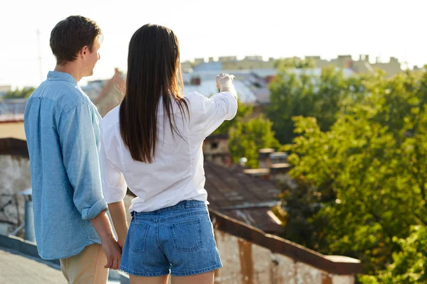 在屋顶约会中 年轻女子在牵着男友的时候指着向前 — 图库照片