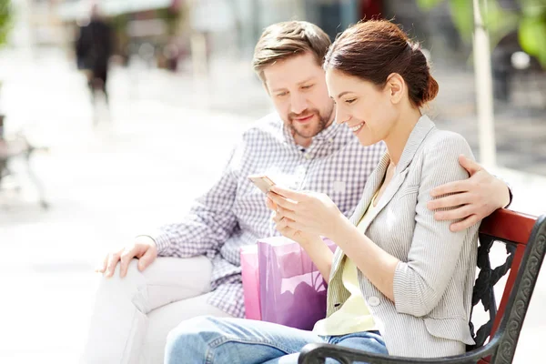 愉快的妇女与智能手机阅读消息或通知后 与她的丈夫附近购物 — 图库照片