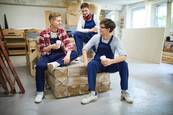 コーヒーカップをパッケージされた木製の板の上に座り 休憩時間にコーヒーを飲みながらコミュニケーションを取る若い男たちを笑顔に — ストック写真