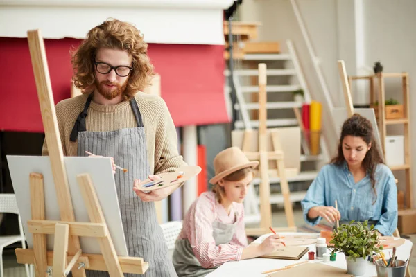 Serious Guy Palette Paintbrush Painting Easel Two Girls Sketching Background — Stock Photo, Image