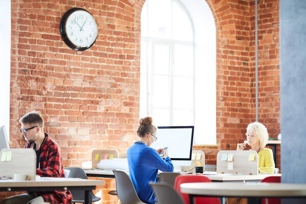 Современные менеджеры в повседневной одежде сидят на своих рабочих местах в рабочий день в офисе
