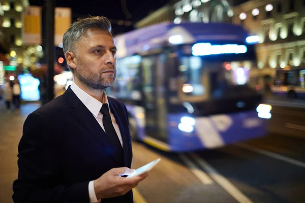 Poważny Biznesmen Smartfonem Zamawiając Taksówkę Stojąc Przy Drodze Wieczorem — Zdjęcie stockowe