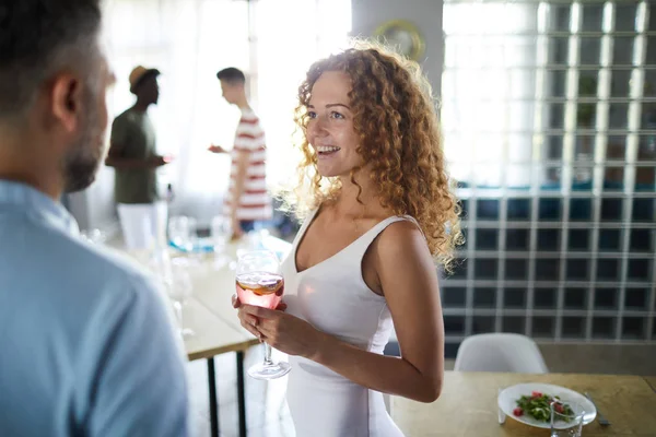漂亮的年轻女子与一杯玫瑰色的饮料看着一个朋友在家庭聚会上交谈 — 图库照片